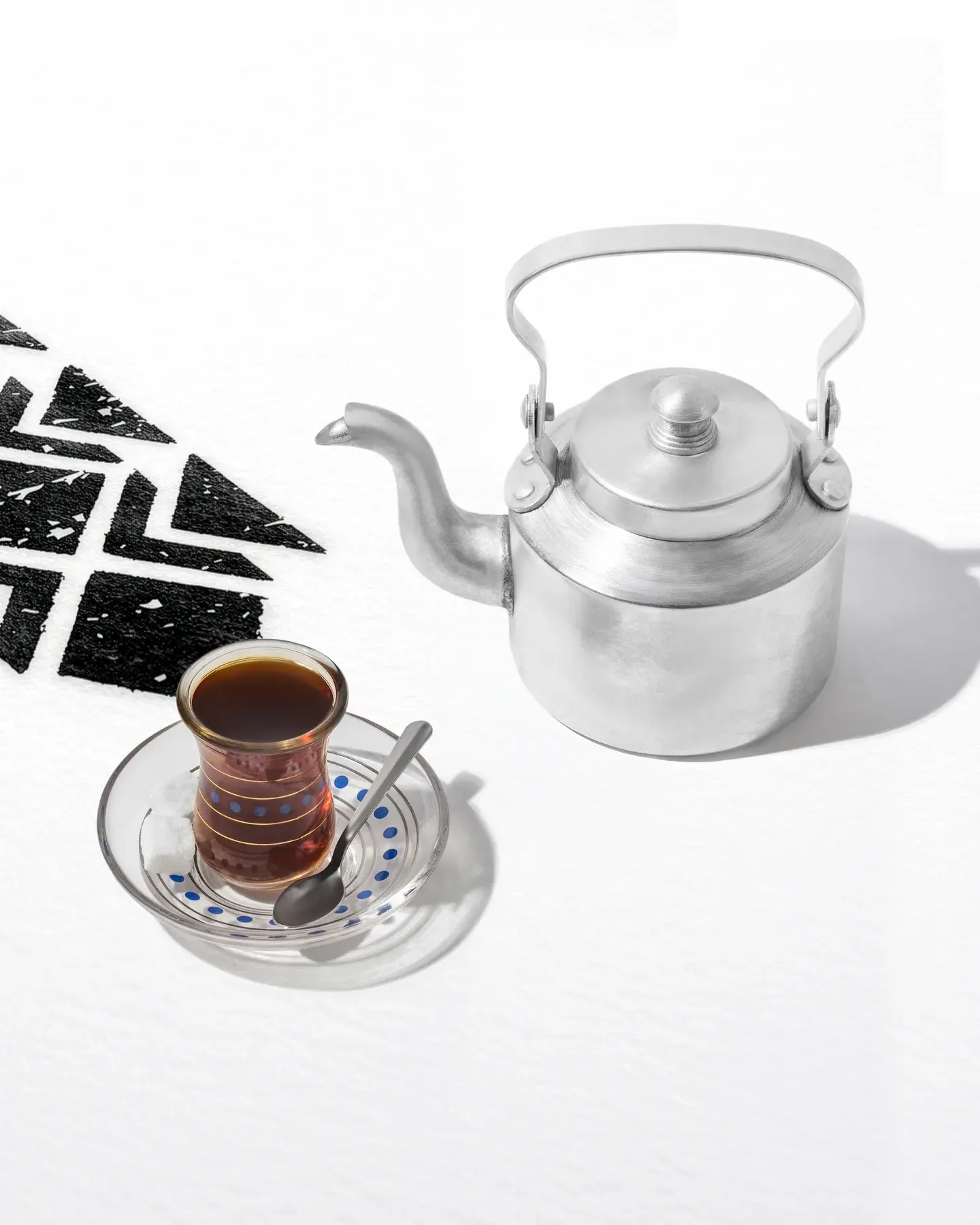 An aluminium teapot beside a glass of tea.