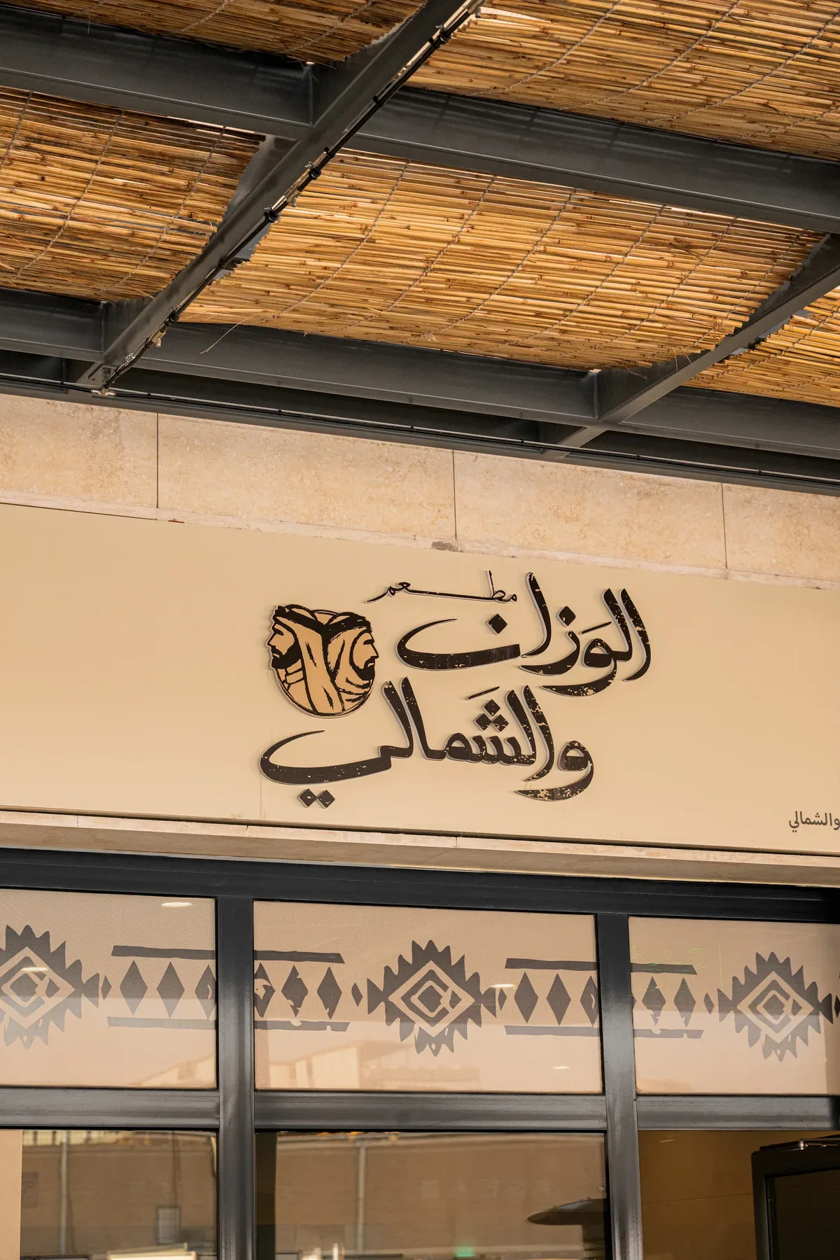 The restaurant sign in Arabic calligraphy under a reed ceiling.
