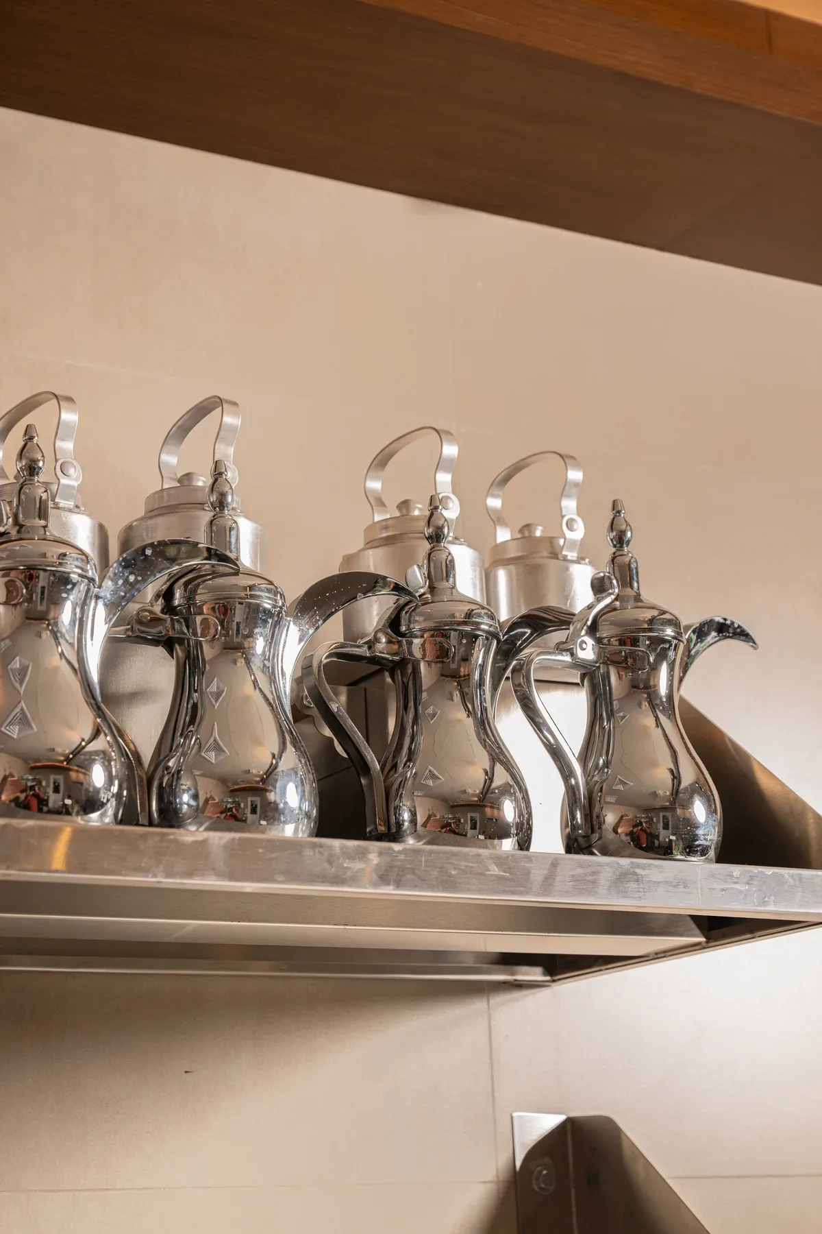 A row of silver dallah coffee pots on a shelf.