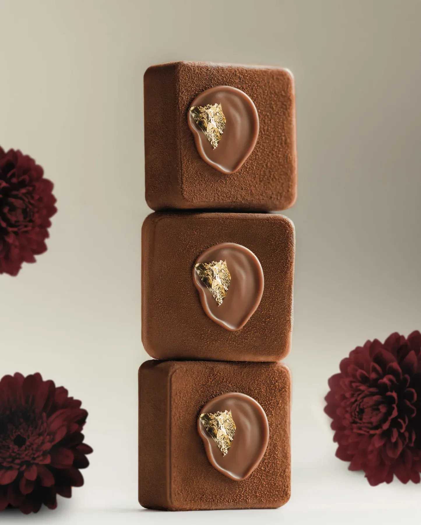 Chocolate cubes with gold leaf stacked between dark dahlias.