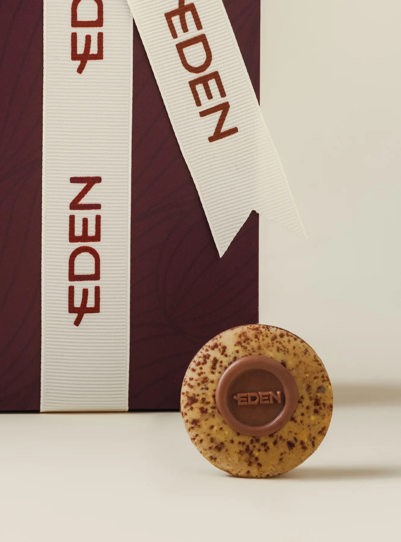 Eden ribbons draped over a cream set beside a stamped round chocolate.