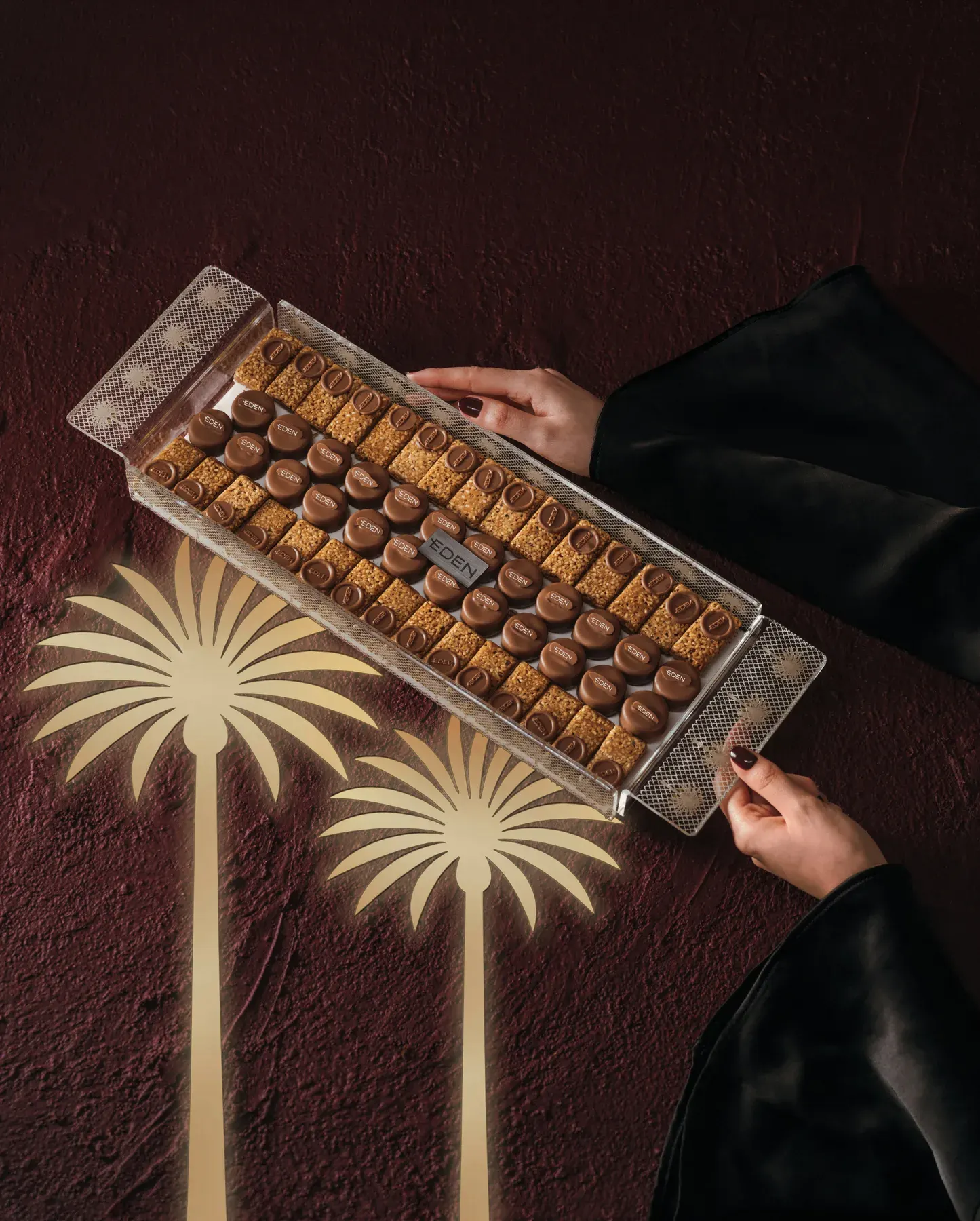 A long tray of chocolates carried across the set under palm tree shadows.