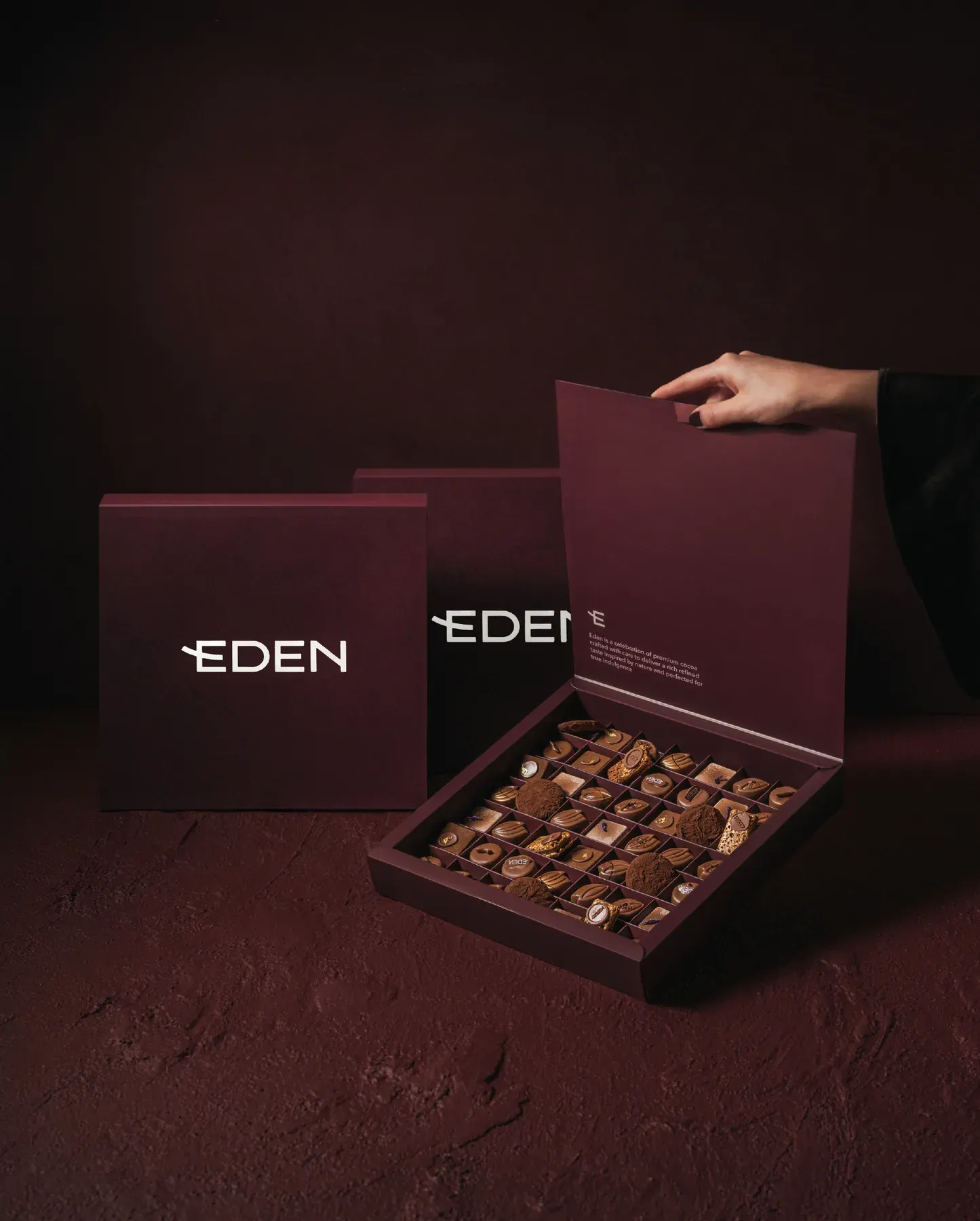 A hand lifting the lid from a box of Eden chocolates.