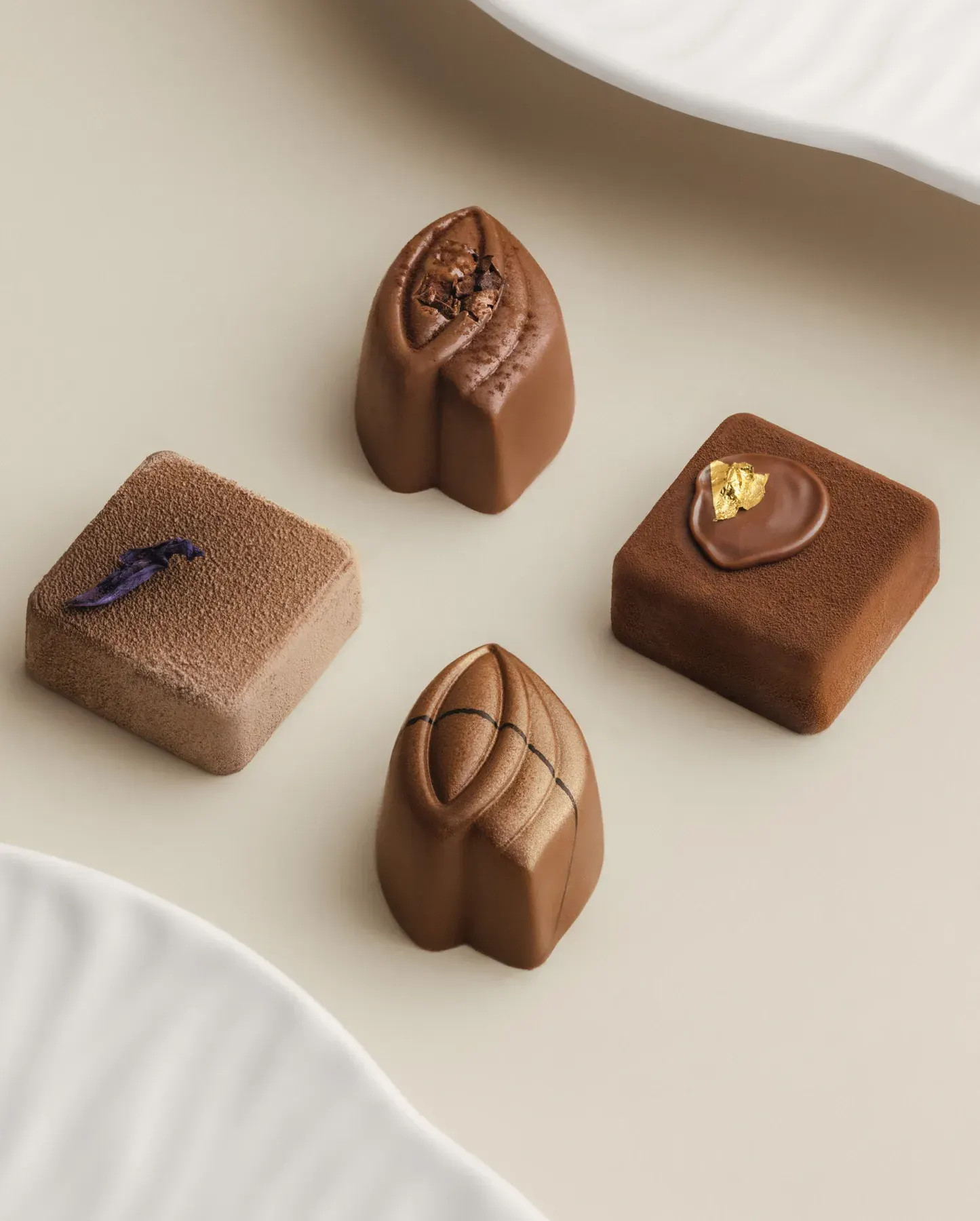 Four sculpted Eden pralines, one finished with gold leaf, on a cream surface.