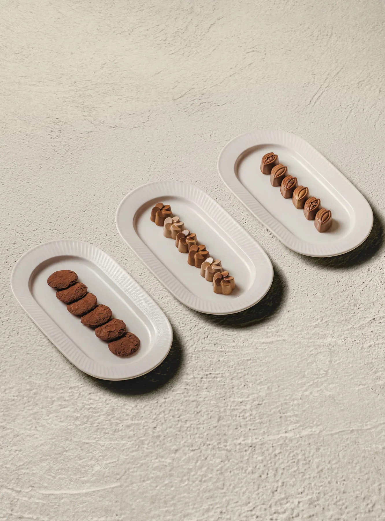 Three white oval dishes, each holding a row of one chocolate.