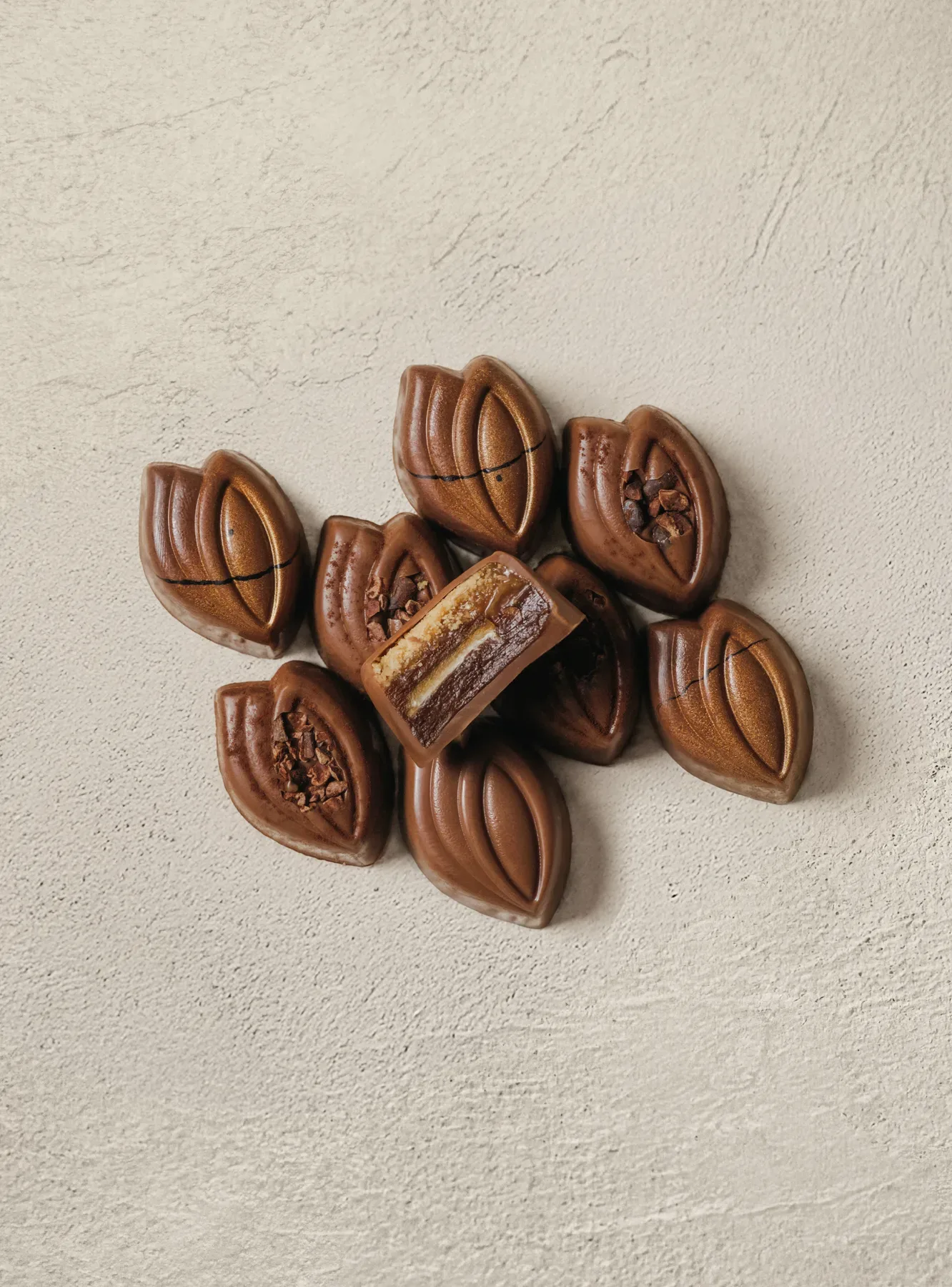 Cocoa pod pralines gathered on pale stone, one cut open.