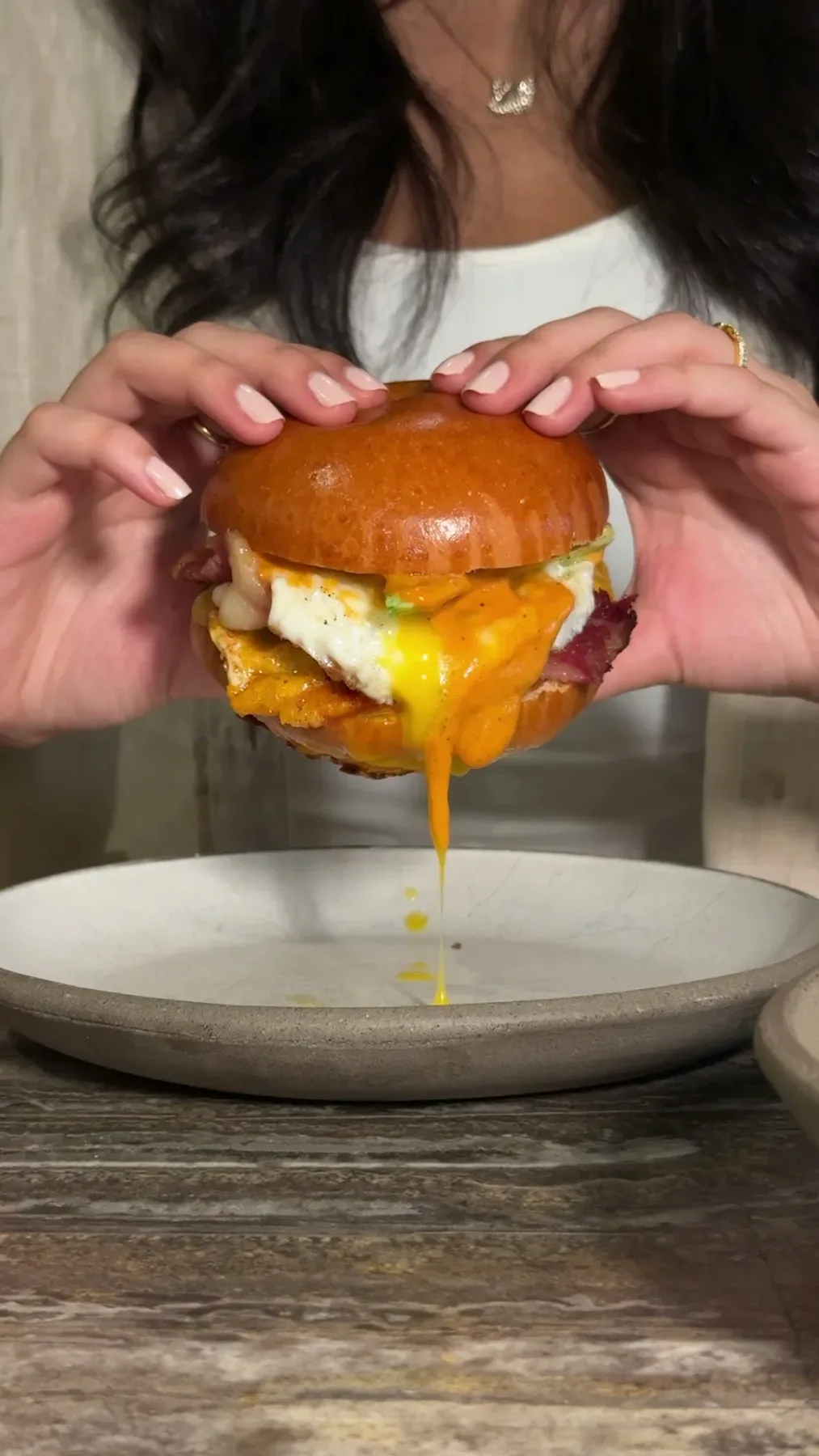 A burger held over a plate as the egg yolk runs.