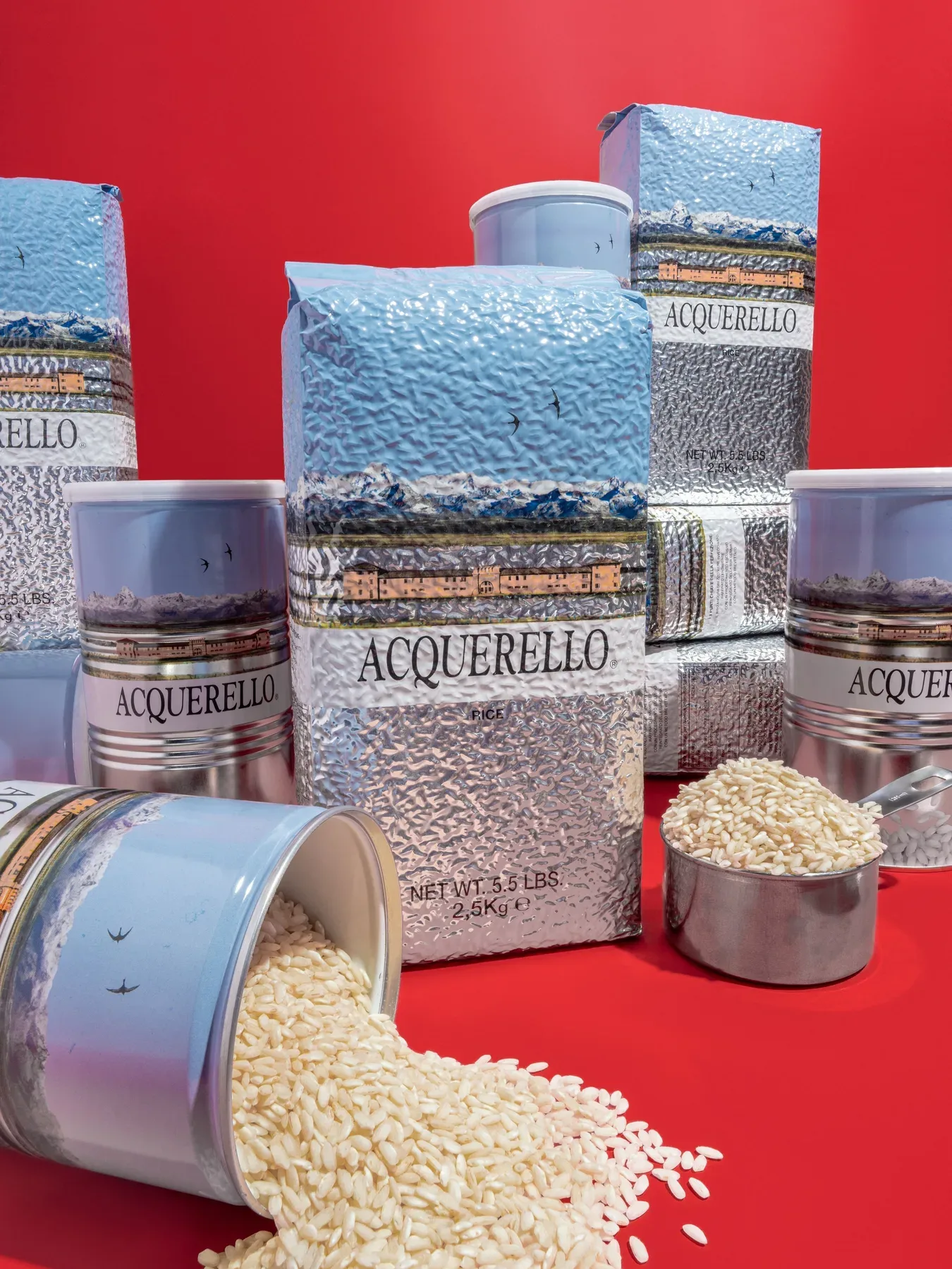 Tins and sacks of Acquerello rice on red, with rice spilling from an open tin.