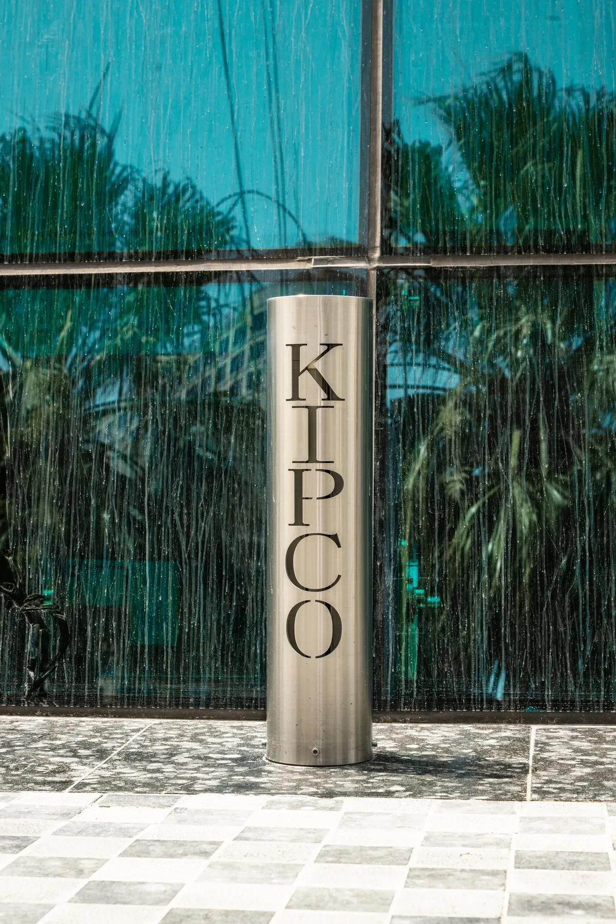 The KIPCO totem against the glass, with palms in the reflection.
