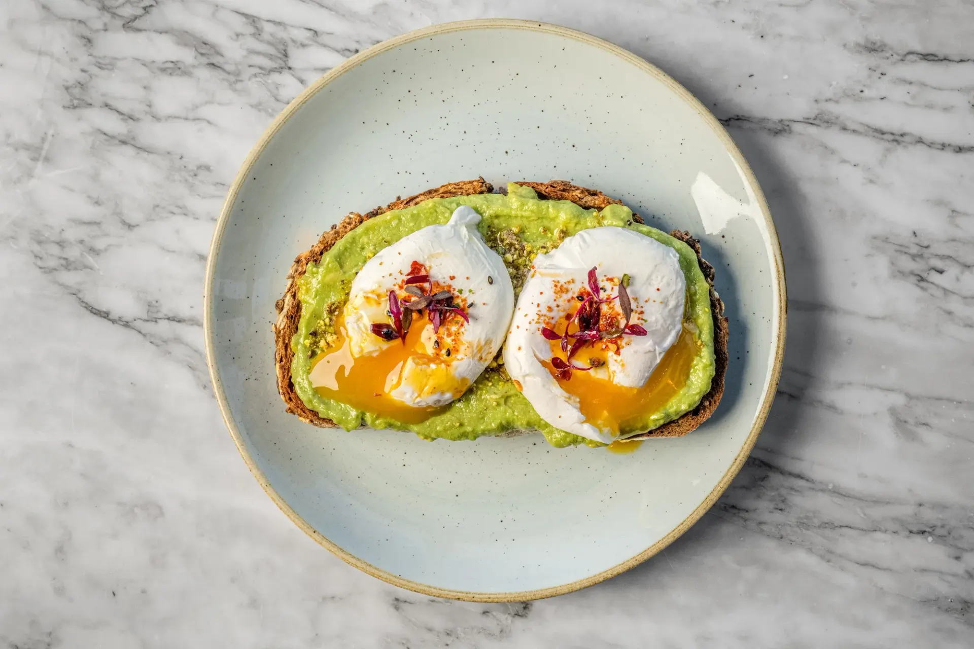 Avocado toast with two poached eggs, overhead on marble.