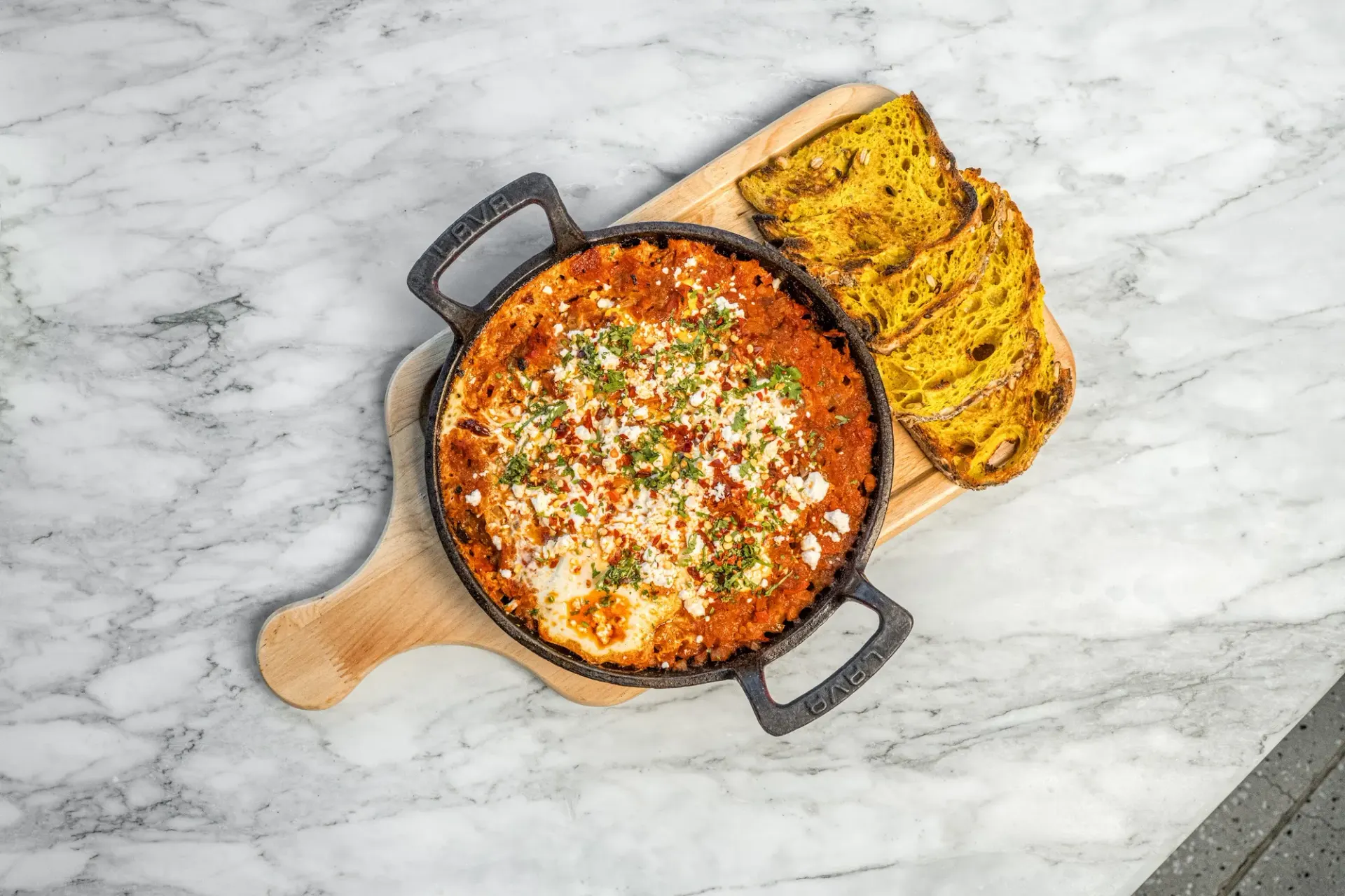 A shakshuka skillet with cornbread on a wooden board.