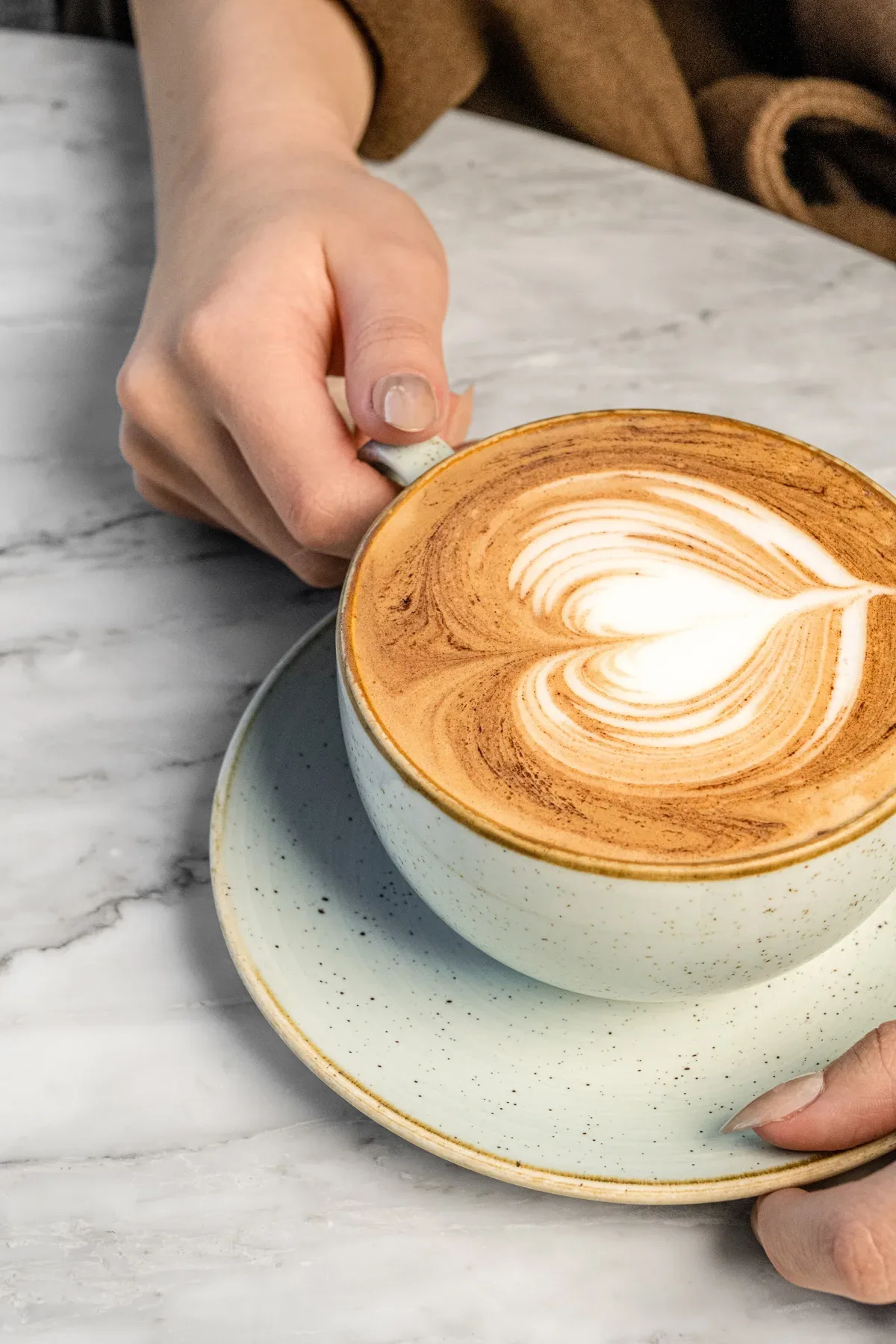 A latte with heart shaped art lifted from its saucer.
