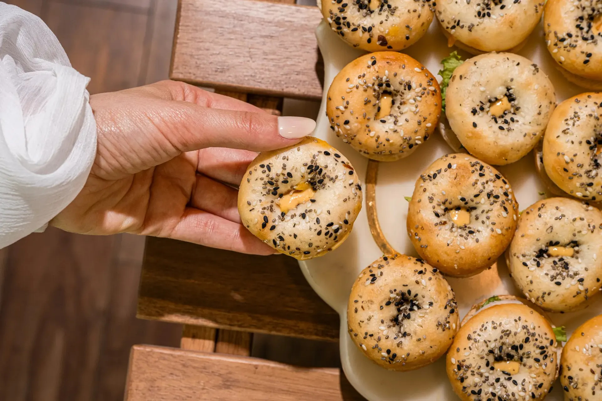A hand reaching over a platter of seeded bagels.