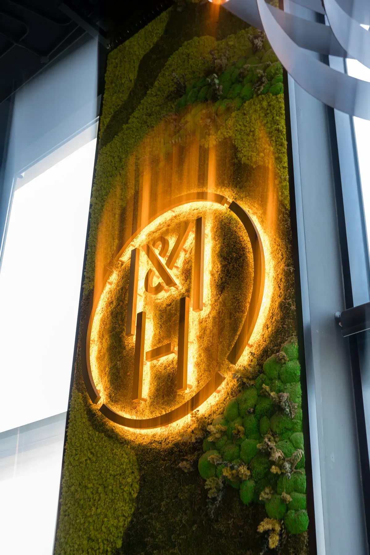 The gold M&H monogram in neon on a moss wall.