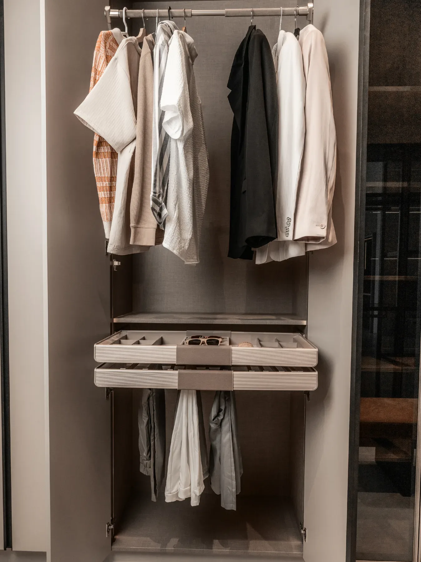 A wardrobe bay with hanging garments and a pull out tray.