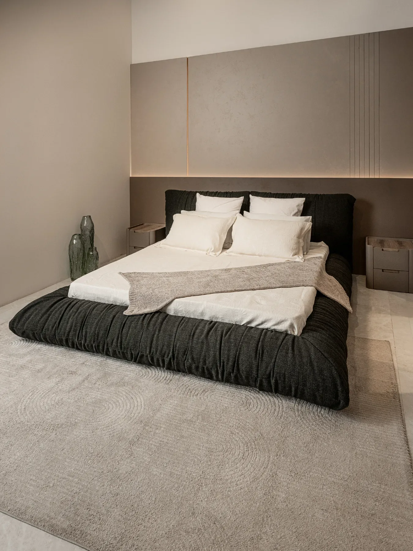 A bedroom with a low bed against a panelled headboard wall.