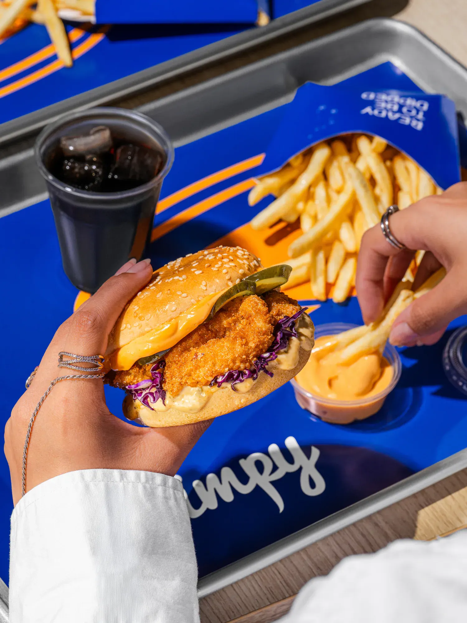 The burger held over the tray, with the fries and the dip still in frame.