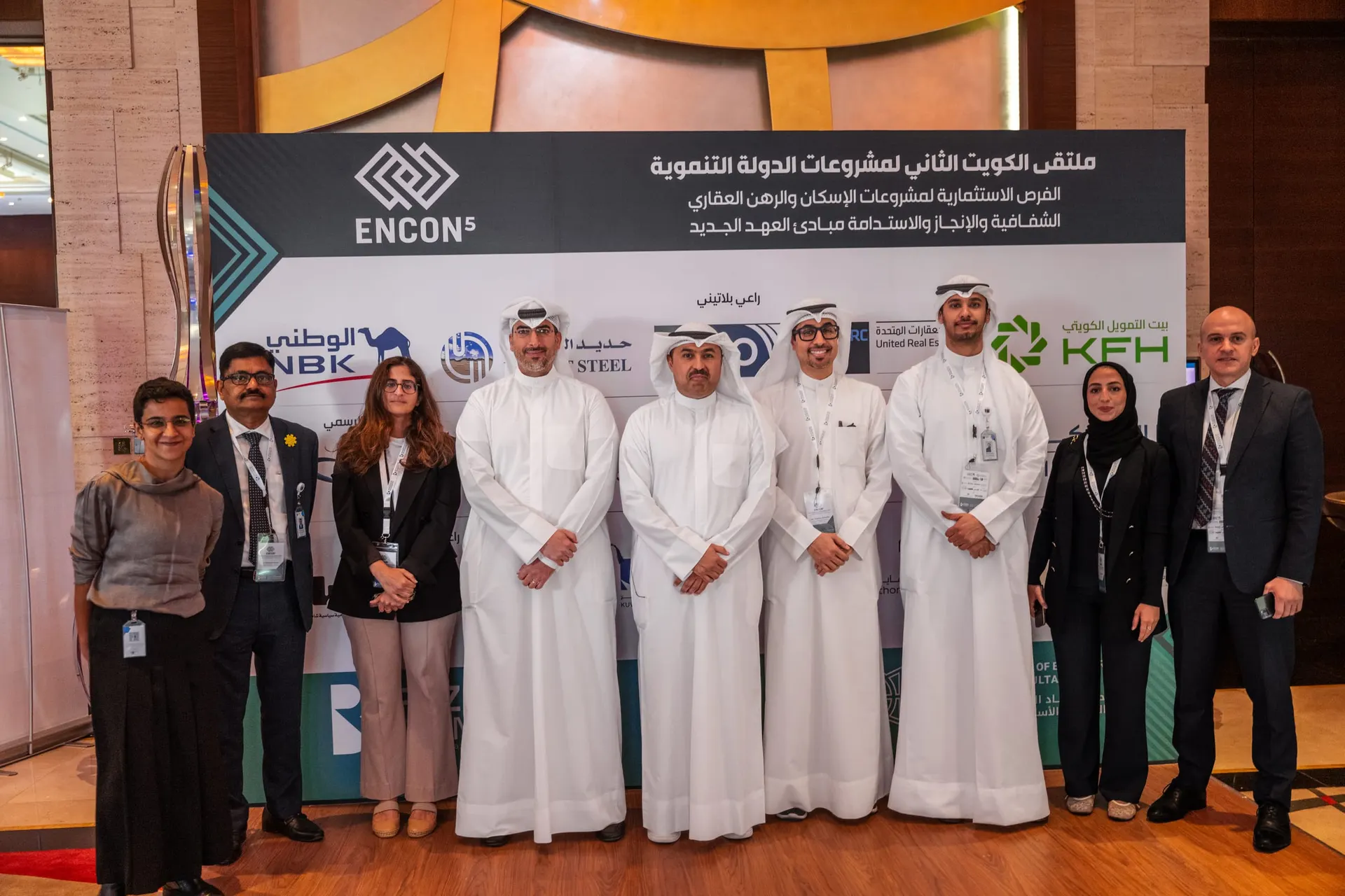 Nine delegates with conference lanyards pose before the ENCON 5 sponsor wall, which reads "Second Kuwait Forum for State Development Projects".