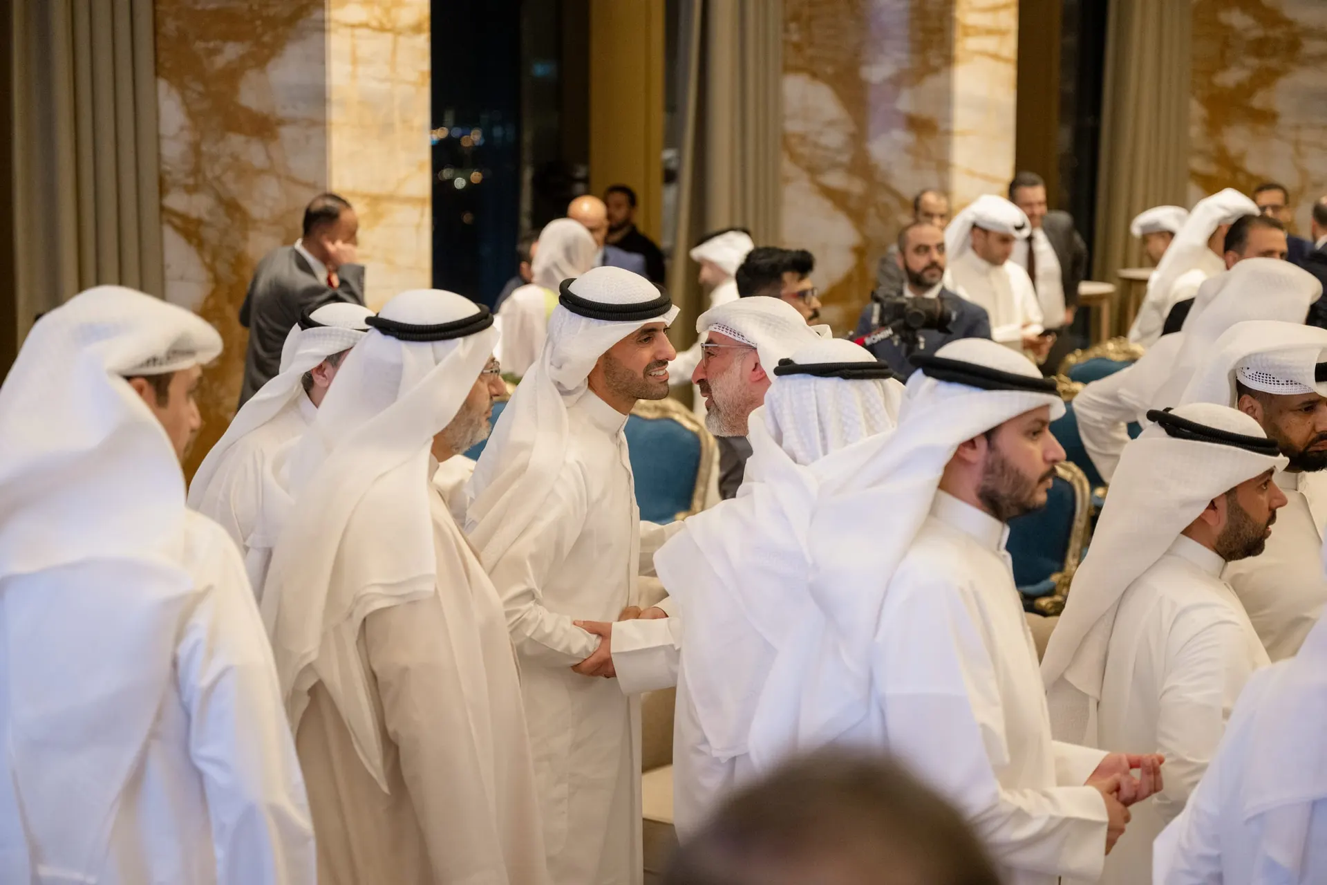 Guests in Kuwaiti dress exchange handshakes and congratulations in the hall after the signing.