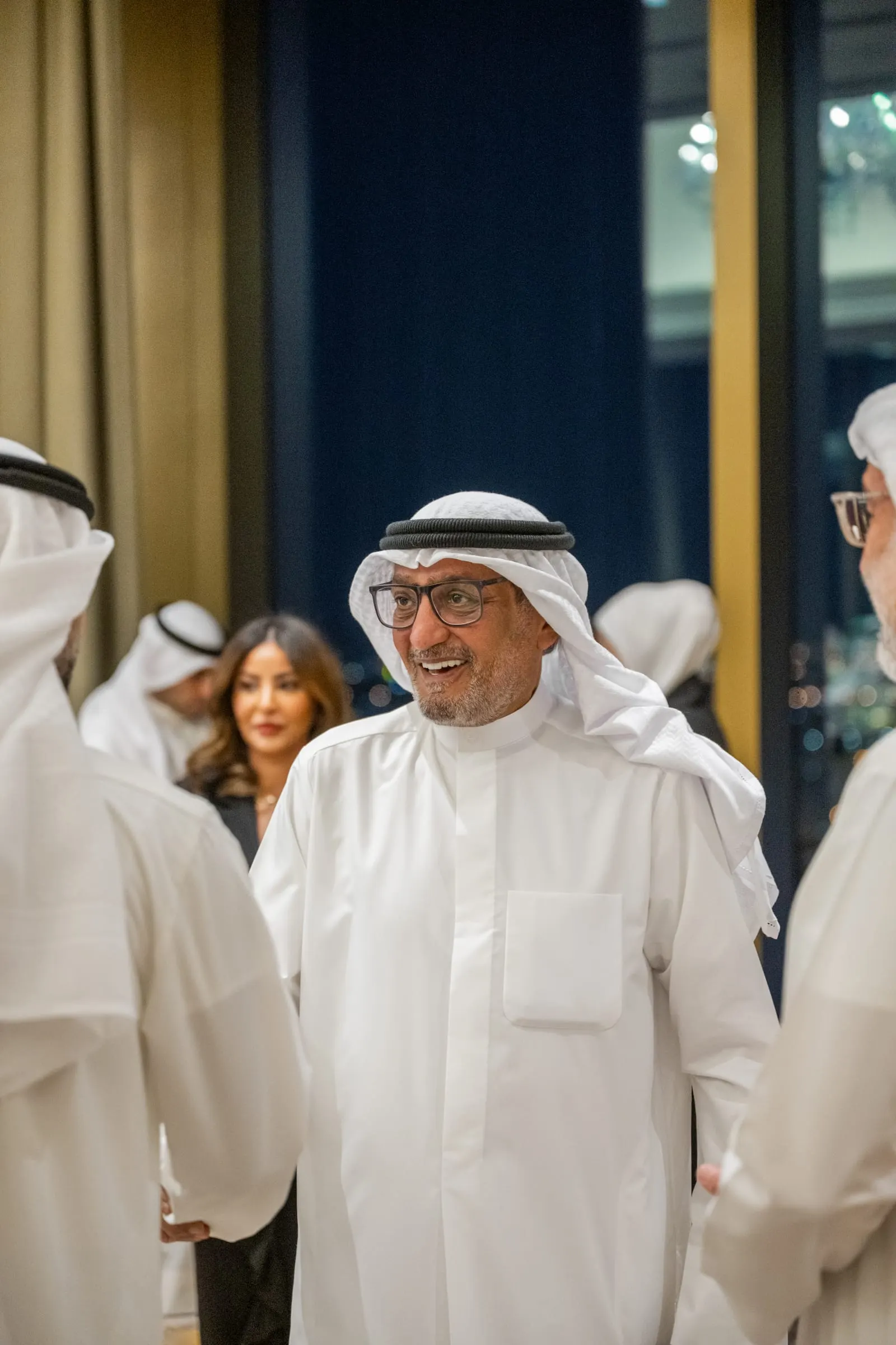 A smiling guest in glasses and Kuwaiti dress greets other guests in the reception area before the ceremony.