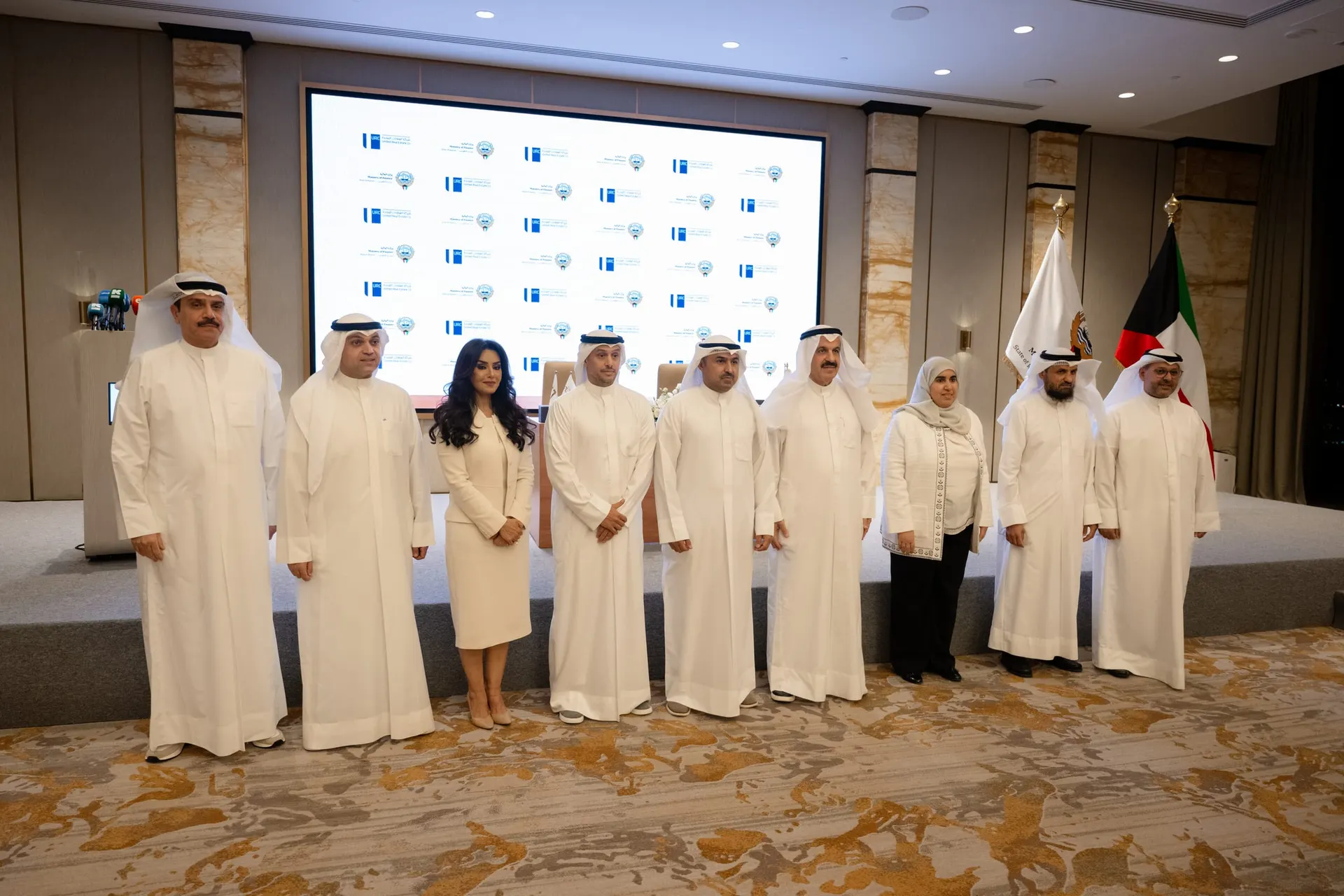 Nine guests pose for a group photo in front of a screen repeating the United Real Estate Company and Ministry of Finance logos.